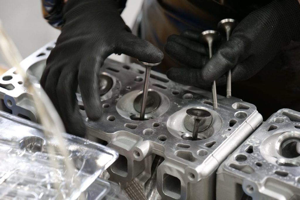 Close-up of mechanics hands working on engine cylinder head assembly with valves.